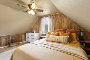 Bedroom featuring wooden walls, a textured ceiling, light wood-type flooring, and a ceiling fan