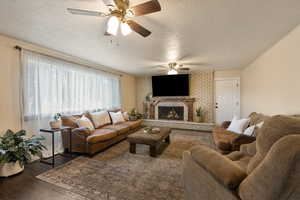 Living area with a textured ceiling, dark wood-style flooring, a brick fireplace, and ceiling fan