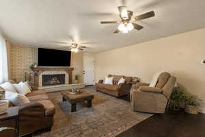 Living area with a textured ceiling, wood finished floors, a brick fireplace, ceiling fan, and brick wall