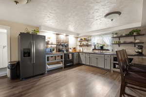 Kitchen with open shelves, stainless steel appliances, a textured ceiling, gray cabinetry, and dark wood-style flooring