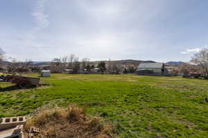 View of green lawn with a mountain view, an outbuilding, and a rural view