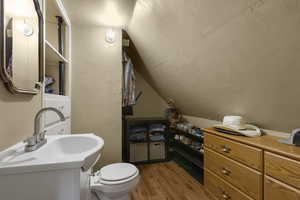 Half bathroom with light wood-style floors and vaulted ceiling