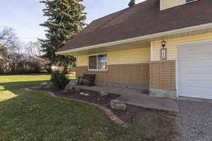 View of side of property with a lawn, brick siding, roof with shingles, and a garage