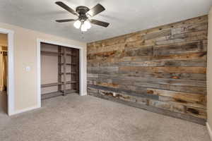 Unfurnished bedroom featuring carpet floors, wooden walls, ceiling fan, a textured ceiling, and a closet