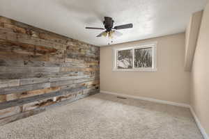 Empty room featuring wood walls, ceiling fan, carpet floors, and a textured ceiling