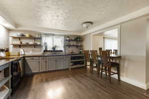 Kitchen with gray cabinets, open shelves, black range with electric stovetop, dark wood-style flooring, and a textured ceiling