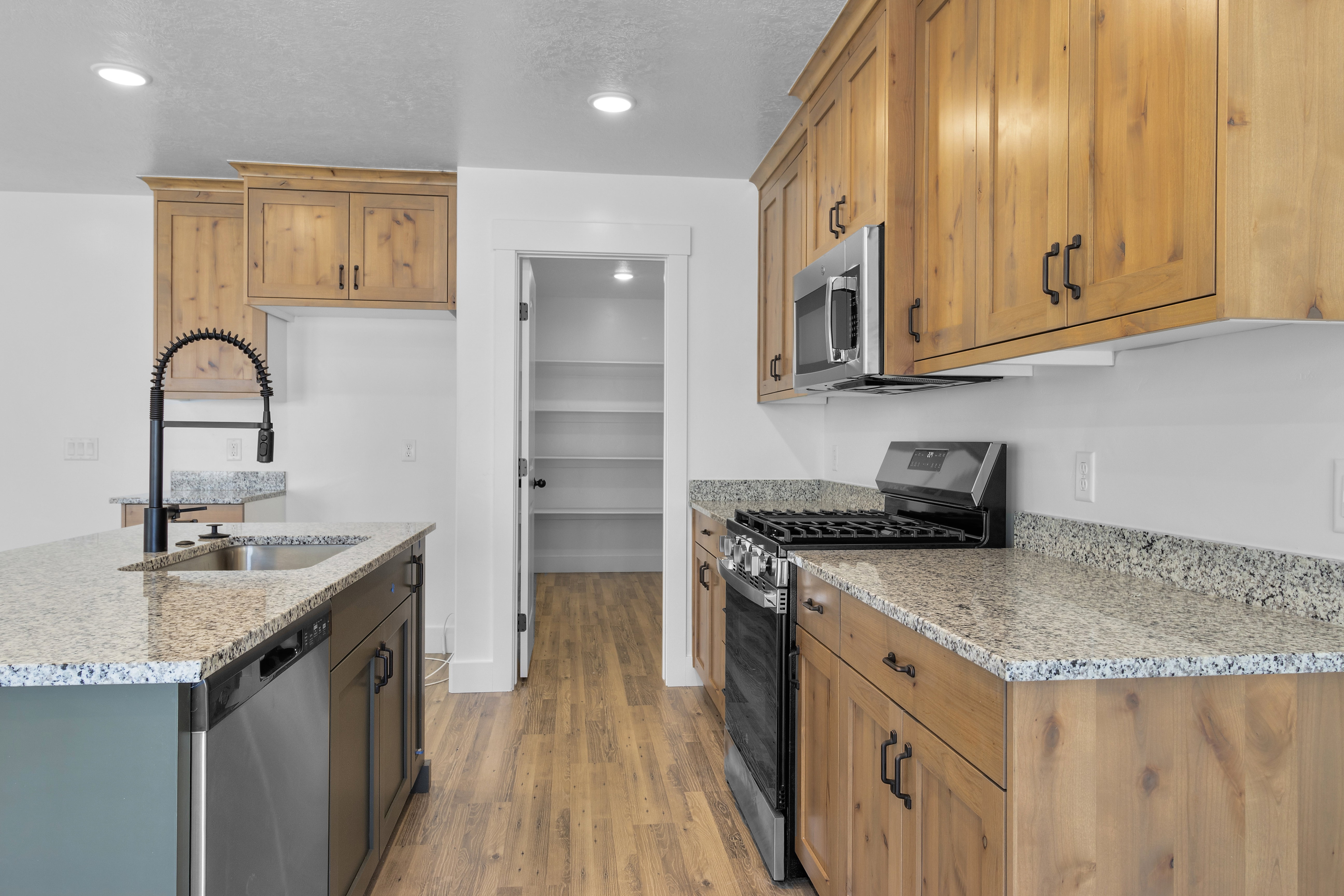 Kitchen featuring stainless steel appliances, light stone countertops, light wood-type flooring, recessed lighting, and an island with sink