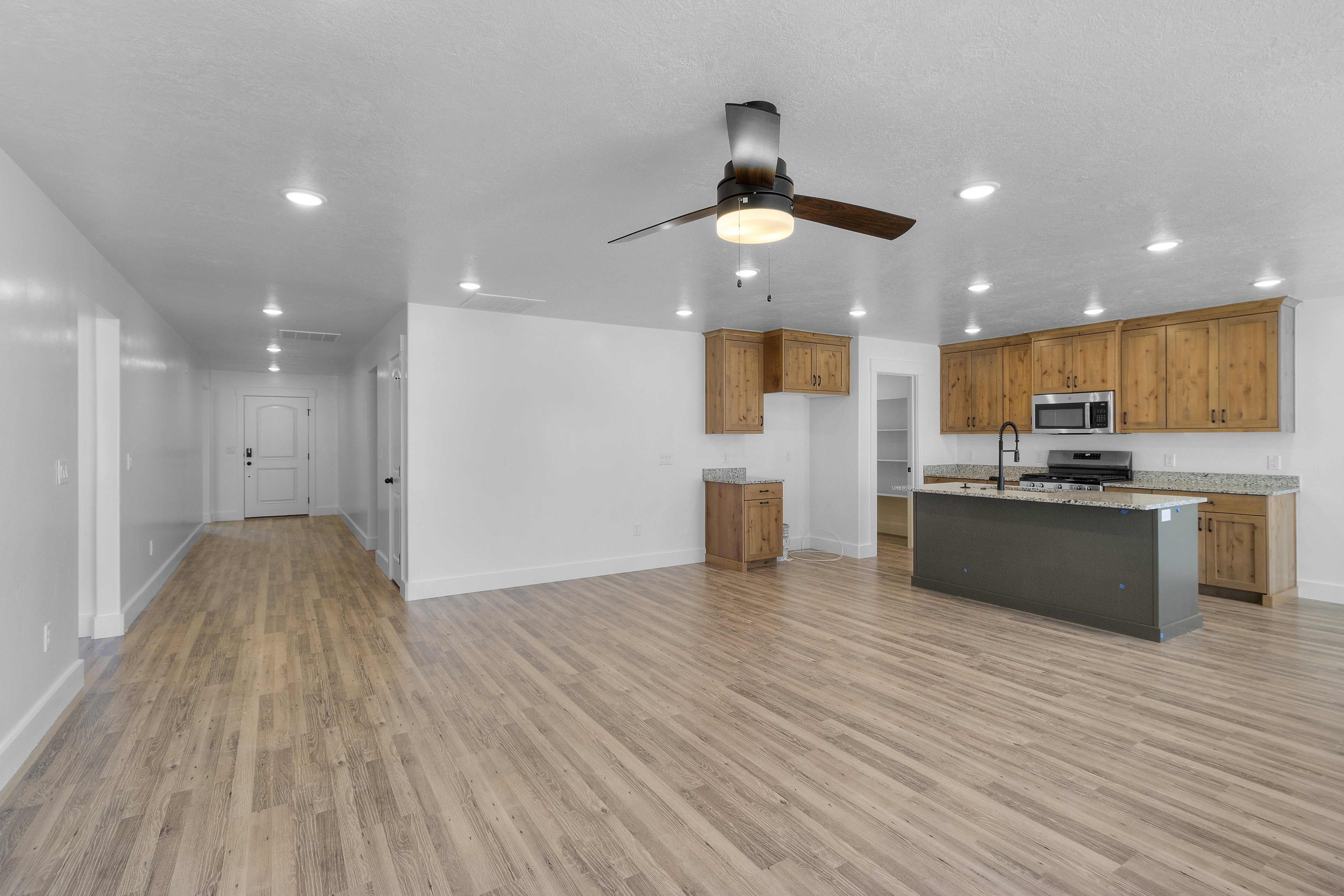 Kitchen with wood finish cabinets, ceiling fan, an island with sink, light wood-style floors, and open floor plan