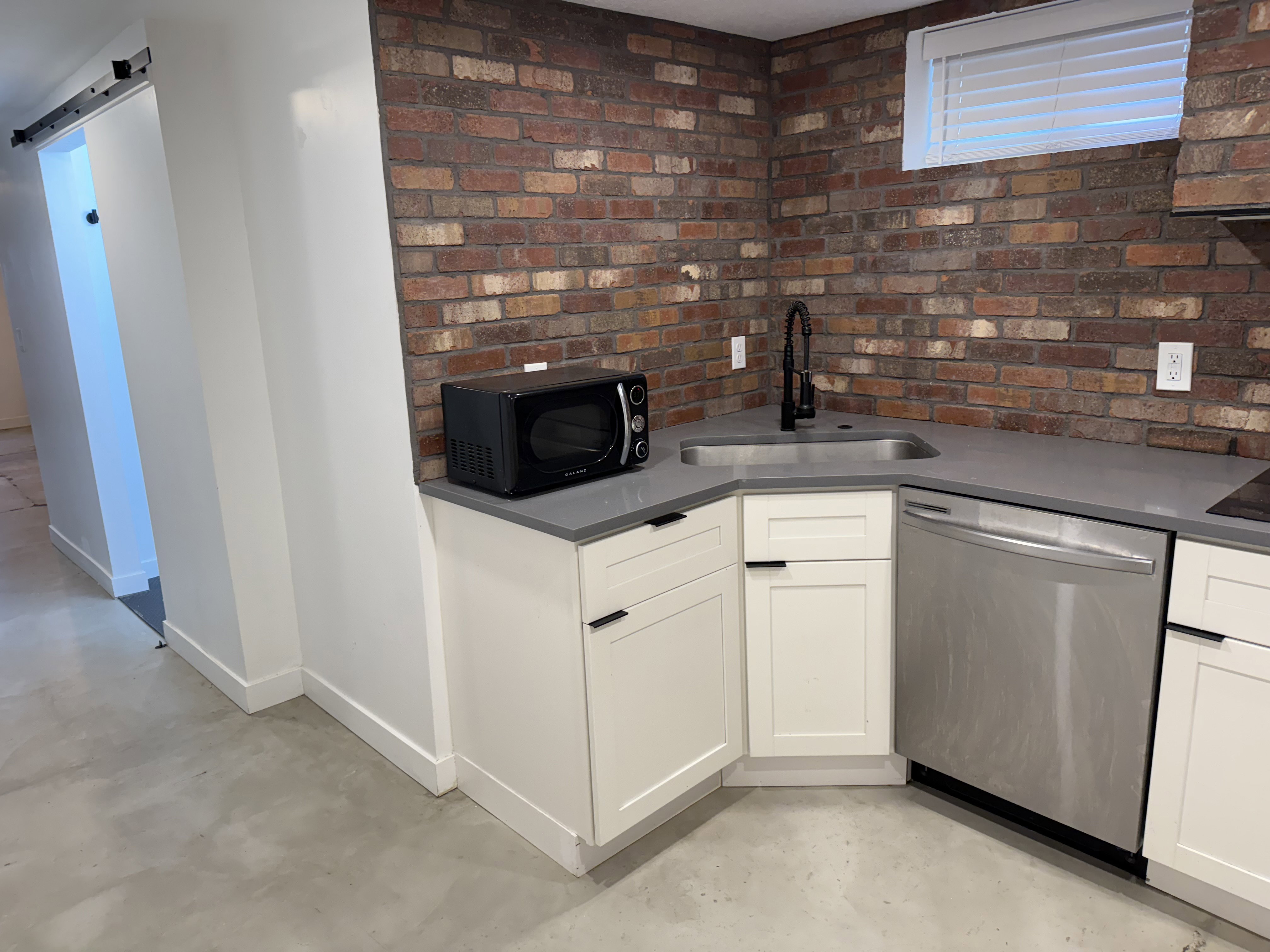 Kitchen with dishwasher, concrete flooring, white cabinetry, black microwave, and brick wall