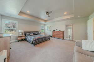 Bedroom with light colored carpet, recessed lighting, ceiling fan, and a raised ceiling