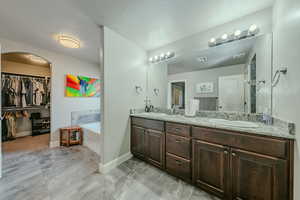 Full bathroom featuring double vanity, a walk in closet, a garden tub, and light marble finish flooring