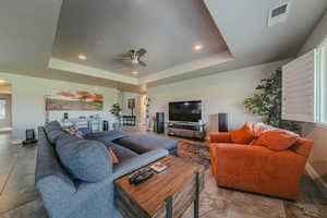 Living area featuring a raised ceiling, a ceiling fan, and recessed lighting