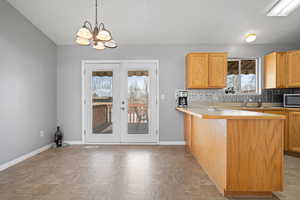 Kitchen featuring a peninsula, stone finish flooring, backsplash, and suspended lighting