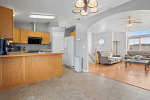 Kitchen with a peninsula, arched walkways, a ceiling fan, open floor plan, and white fridge with ice dispenser