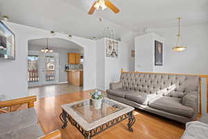 Living area featuring arched walkways, ceiling fan, lofted ceiling, light wood finished floors, and hanging lights