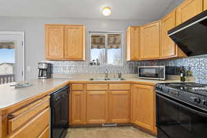 Kitchen featuring black appliances, light countertops, extractor fan, a peninsula, and tasteful backsplash