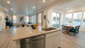 Kitchen featuring light wood-style floors, open floor plan, stainless steel dishwasher, white cabinetry, and recessed lighting