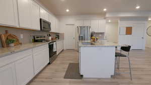 Kitchen with white cabinetry, stainless steel appliances, light stone counters, a kitchen island with sink, and recessed lighting