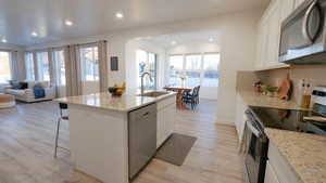 Kitchen featuring stainless steel appliances, light wood-type flooring, white cabinets, open floor plan, and light stone counters