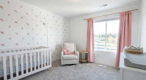 Bedroom featuring a crib, light colored carpet, and wallpapered walls