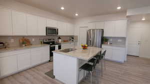 Kitchen featuring stainless steel appliances, white cabinets, tasteful backsplash, a breakfast bar, and recessed lighting