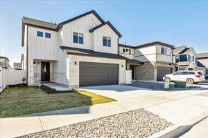 View of front of home with board and batten siding, an attached garage, concrete driveway, and stone siding