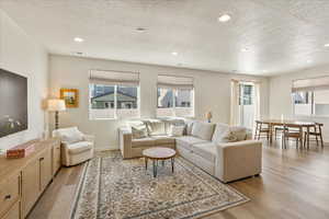 Living area with light wood-style floors, recessed lighting, a textured ceiling, and healthy amount of natural light