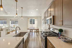 Kitchen with stainless steel appliances, open floor plan, light wood-type flooring, pendant lighting, and a textured ceiling
