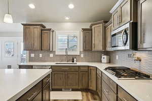 Kitchen with stainless steel appliances, light stone counters, light wood-type flooring, decorative backsplash, and hanging light fixtures