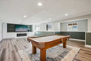 Playroom with wainscoting, billiards, light wood-style floors, recessed lighting, and a glass covered fireplace
