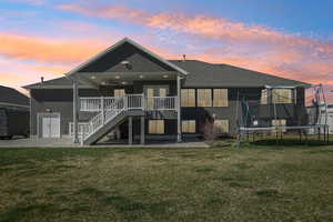 Back of house at dusk with a patio, a ceiling fan, a yard, a trampoline, and stucco siding
