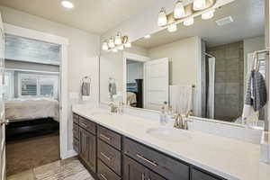 Ensuite bathroom featuring double vanity, a tile shower, recessed lighting, and a textured ceiling