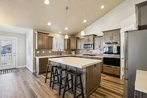 Kitchen featuring stainless steel appliances, a kitchen bar, vaulted ceiling, dark wood finished floors, and a center island