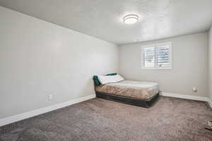 Carpeted bedroom featuring a textured ceiling and baseboards