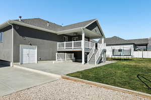 Back of house featuring ceiling fan, a trampoline, roof with shingles, a patio area, and a deck