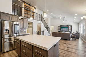 Kitchen featuring stainless steel fridge with ice dispenser, dark wood finish cabinetry, a kitchen island, light stone countertops, and a high textured ceiling
