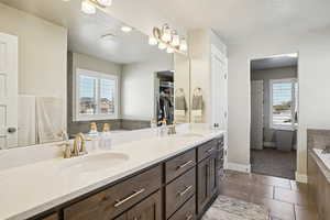 Full bathroom featuring a garden tub, double vanity, dark tile patterned floors, and a textured ceiling