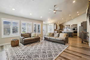 Living room with dark wood-style floors, a chandelier, ceiling fan, and a high textured ceiling