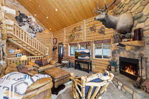 Living area with a stone fireplace, carpet flooring, recessed lighting, log walls, and a vaulted wood ceiling
