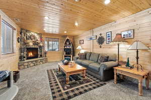 Living area with wood walls, recessed lighting, carpet floors, a stone fireplace, and wooden ceiling