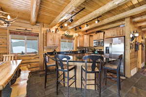 Kitchen featuring stainless steel appliances, a wood ceiling with exposed beams, a kitchen bar, a center island, and rail lighting