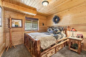 Bedroom with wooden walls, wood ceiling, and dark carpet