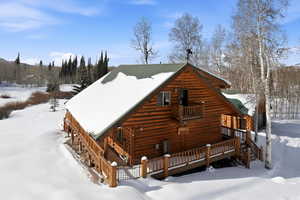 Snow covered back of property with a wooden deck and log exterior