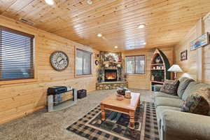 Living room with wooden walls, carpet flooring, wooden ceiling, recessed lighting, and a fireplace