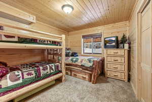 Bedroom featuring wooden walls, wooden ceiling, and light carpet