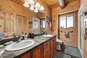 Full bathroom with wood walls, a stall shower, double vanity, dark tile patterned flooring, and a closet