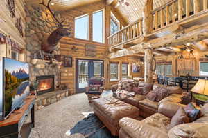 Living room featuring a fireplace, a vaulted wood ceiling, carpet, a ceiling fan, and rustic walls