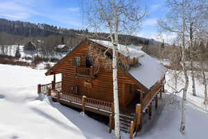 View of snow covered exterior featuring a deck and a wooded view