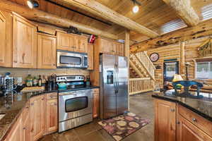 Kitchen featuring log walls, stainless steel appliances, a wood ceiling with exposed beams, dark stone countertops, and wood finish cabinetry