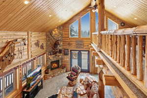 Unfurnished living room with rustic walls, a stone fireplace, ceiling fan, a high ceiling, and recessed lighting